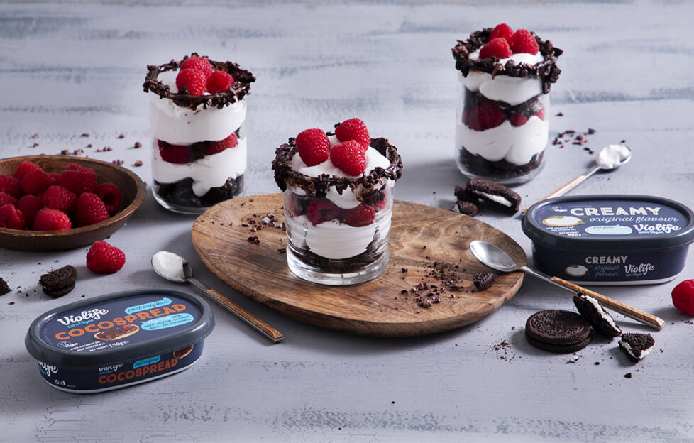 3 glasses of layered cream, chocolate and raspberry desert with tubs of Violife creamy spread and chocolate spread