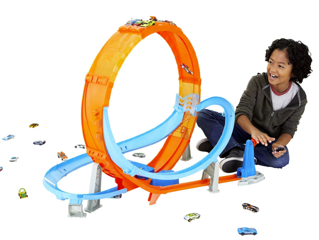 Excited child sitting beside large plastic car track including giant loop the loop