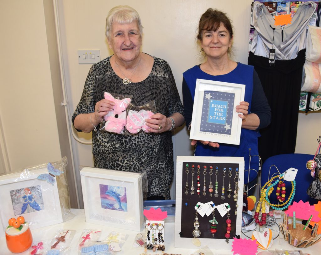 Myrtle Reid, left, holds knitting she created, while Michelle Plant holds a frame made at the church's craft group. All items were for sale on Saturday.