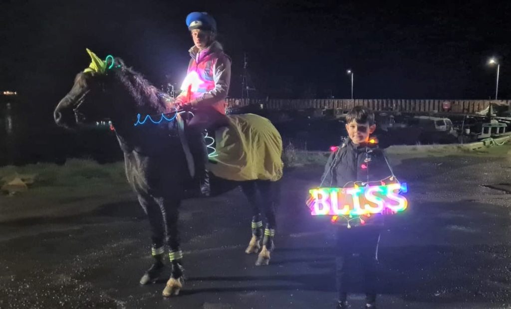 Evan McConnachie holding his illuminated sign and joined by his big sister Leah on her pony Ted.