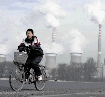 Emissions: A Chinese boy cycles past the cooling towers of a coal-fired power plant in China