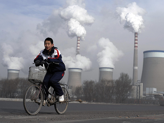 EMISSIONS: A Chinese boy cycles past the cooling towers of a coal-fired power plant in China