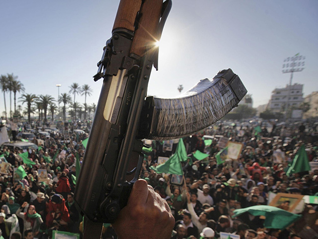 A machine gun in the foreground with lots of people and flags behind