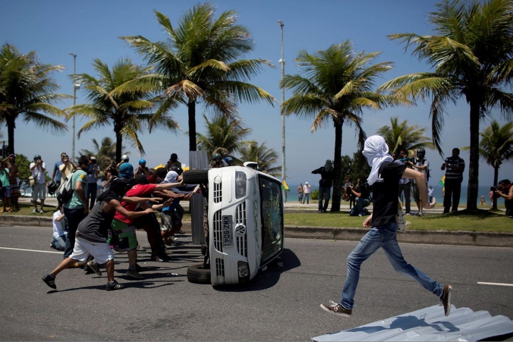 Masked protesters turn over a vehicle from TV Record during a demonstration against the auction of the Libra offshore oil field near the Windsor hotel where the auction is taking place, on Barra da Tijuca beach in Rio de Janeiro, Brazil,