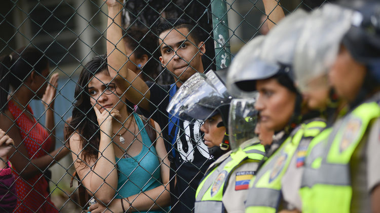 Spectators look on as Bolivarian National Police stand guard near the Central University of Venezuela during pro-opposition students marching near the Central University of Venezuela in Caracas, Venezuela, on Thursday, May 26, 2016.