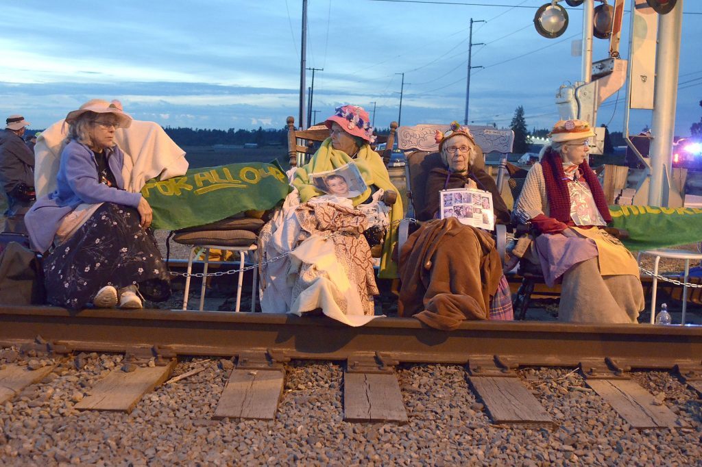 Members of the Seattle Raging Grannies sit in their rocking chairs chained together on the Burlington-Northern Railroad tracks at Farm to Market Road in Skagit County on Friday evening, May 13, 2016, in Burlington, Wash.  From left are Deejay Sherman Peterson, Anne Thureson, Shirley Morrison and Rosy Betz-Zall. Hundreds of people in kayaks and on foot are gathering at the site of two oil refineries in Washington state to call for action on climate change and a fair transition away from fossil fuels. Scott Terrell/Skagit Valley Herald