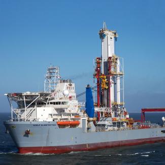 A rig with light grey hull against blue sky