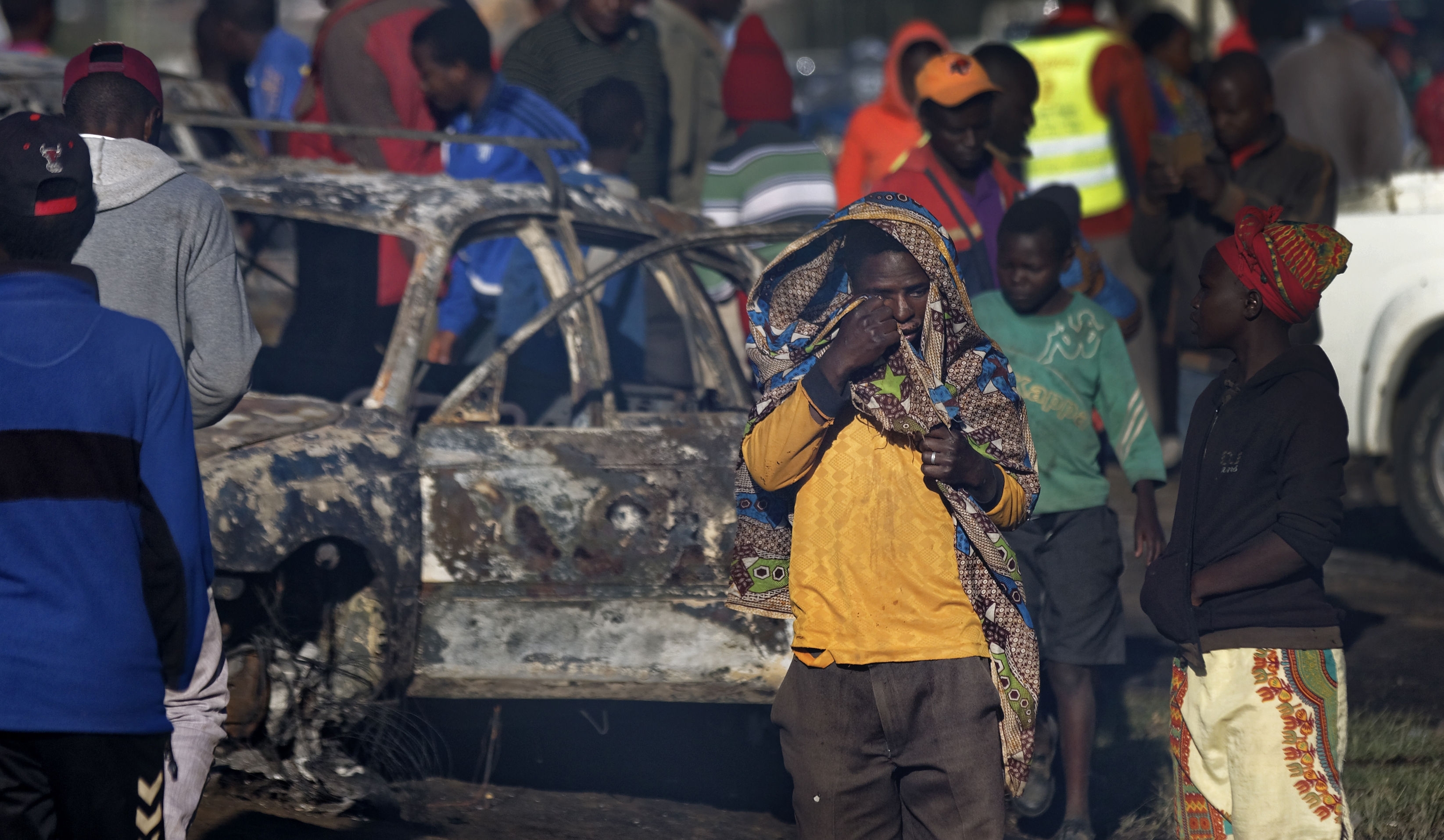 An onlooker wipes his eye as he walks through the still smoldering scene of an accident involving a tanker near Naivasha, in Kenya Sunday, Dec. 11, 2016. The tanker carrying volatile gas slammed into other vehicles and burst into flames on a major road in Kenya, killing dozens of people, officials said early Sunday.