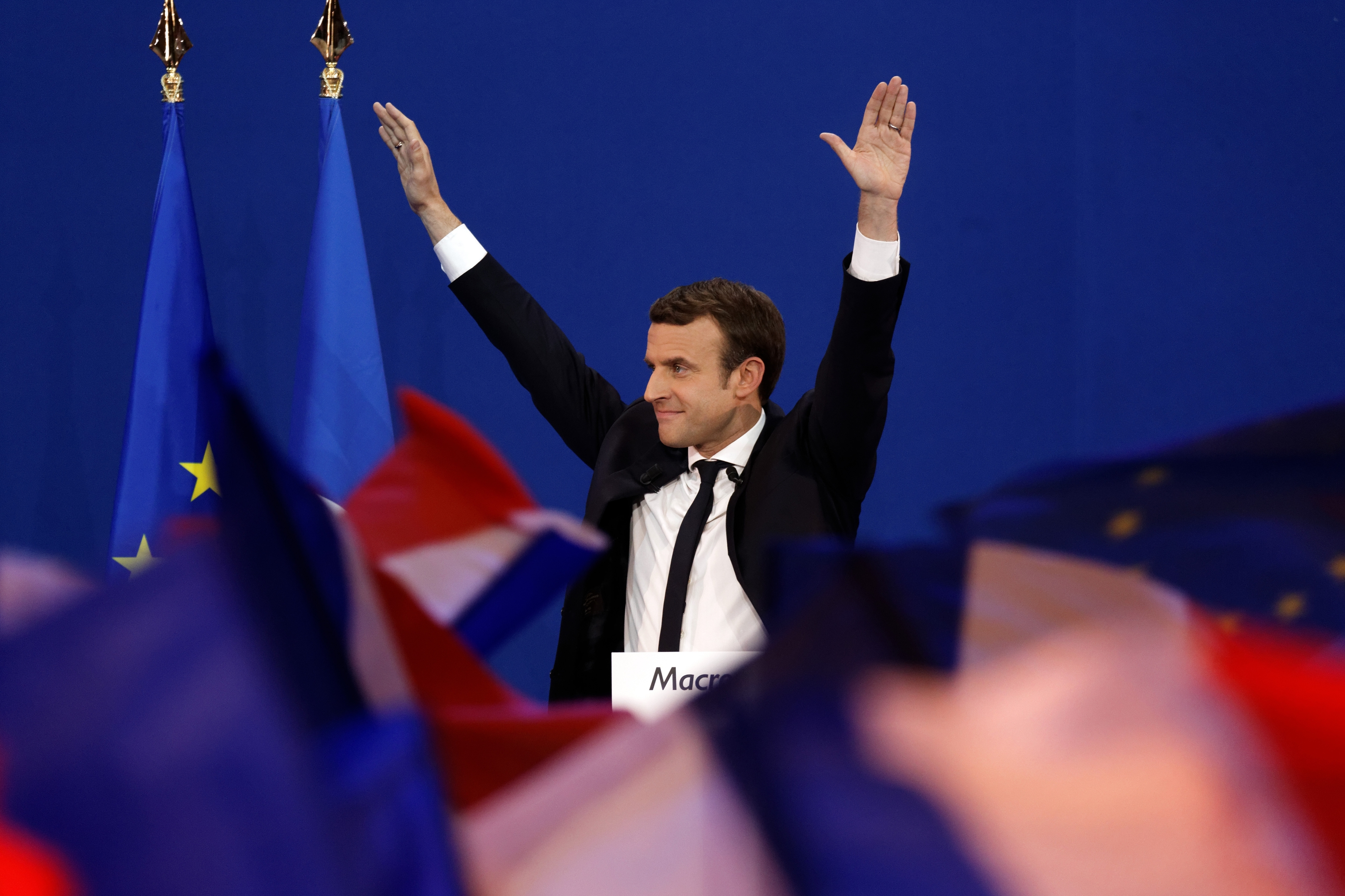 Emmanuel Macron puts his arms up amid French flags