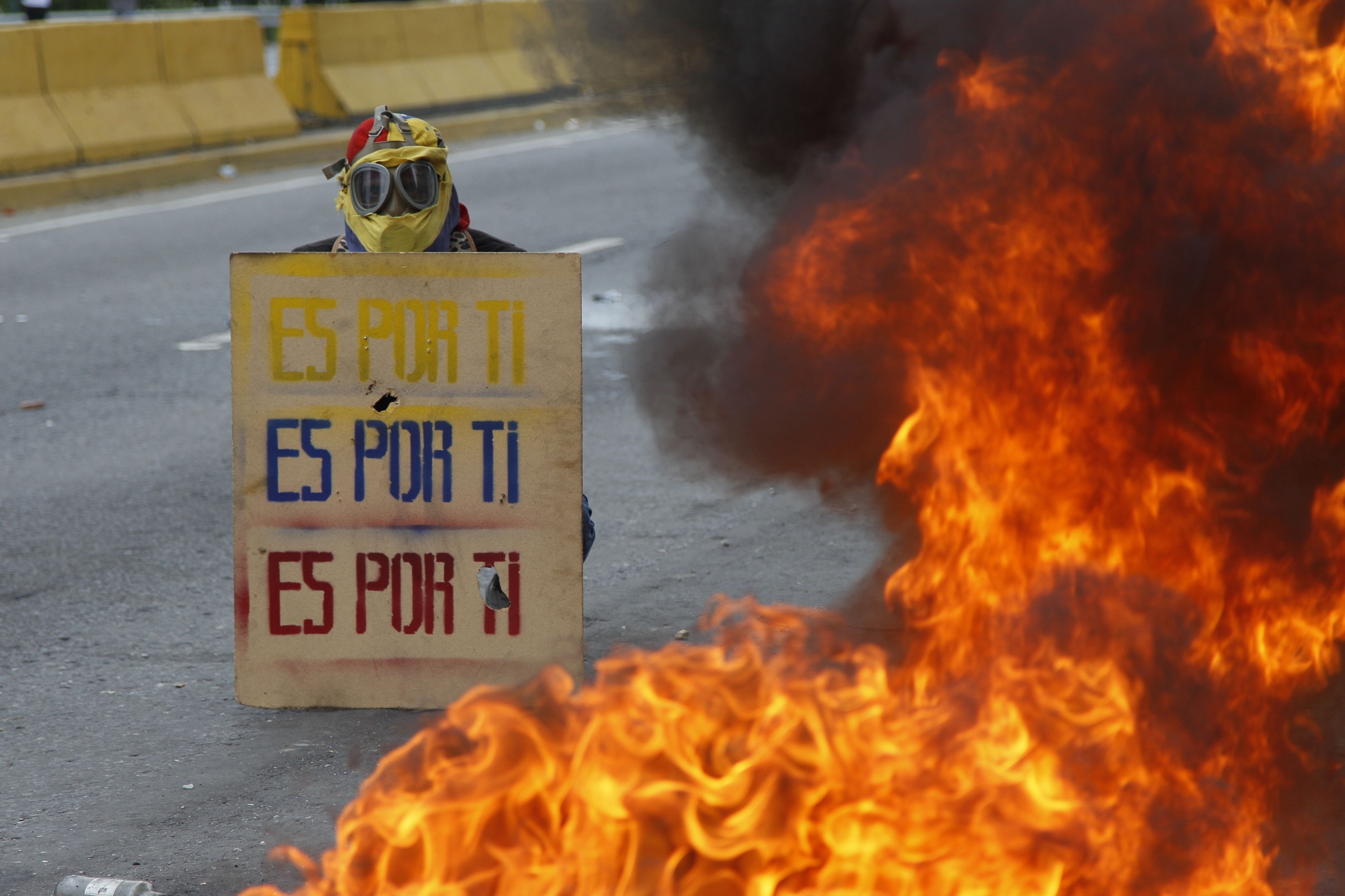 A demonstrator holds a sign that doubles a shield that reads in Spanish "It's for you," during a national sit-in against President Nicolas Maduro, in Caracas, Venezuela, Monday, May 15, 2017.