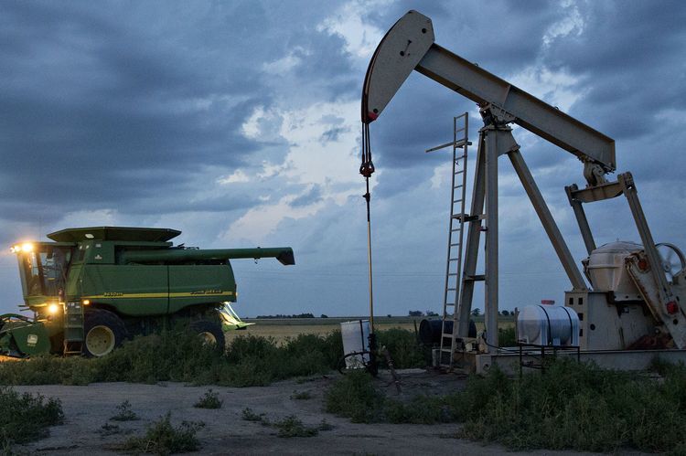 A Deere & Co. John Deere combine harvester drives past a pumpjack in the Bemis-Shutts oil field during the harvest of hard red winter wheat in Plainville, Kansas, U.S. Photographer:  Daniel Acker/Bloomberg