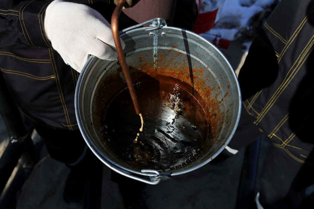Workers use a bucket to collect a sample of crude oil at a multiple well platform, operated by Rosneft PJSC, in the Samotlor oilfield near Nizhnevartovsk, Russia, on Monday, March 20, 2017. Russia's largest oil field, so far past its prime that it now pumps almost 20 times more water than crude, could be on the verge of gushing profits again for Rosneft PJSC. Photographer: Andrey Rudakov/Bloomberg