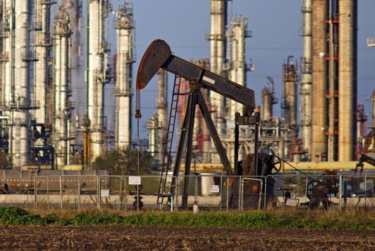 A refinery stands in the background as a pump jack operates in an oil field near Corpus Christi, Texas, U.S., on Thursday, Jan. 7, 2016. Crude oil slid Thursday to the lowest level since December 2003 as turbulence in China, the worlds biggest energy consumer, prompted concerns about the strength of demand. Photographer: Eddie Seal/Bloomberg