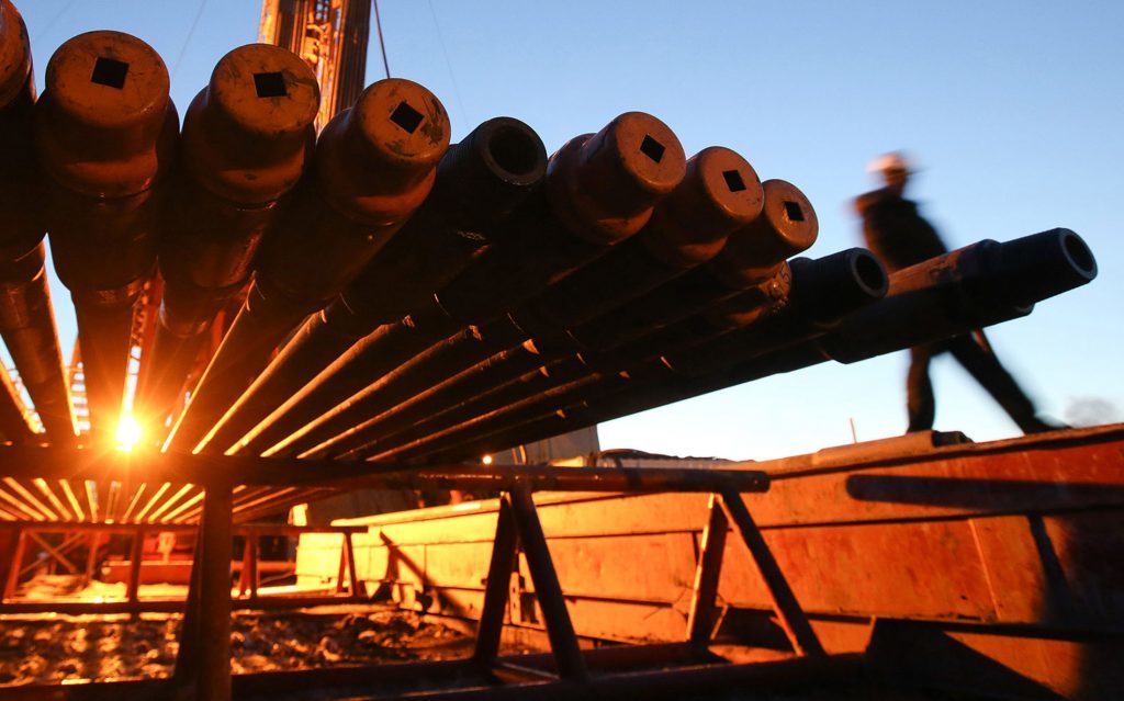 A worker passes an illuminated oil drilling rig and drill pipes, operated by Rosneft PJSC, in the Samotlor oilfield near Nizhnevartovsk, Russia. Photographer: Andrey Rudakov/Bloomberg