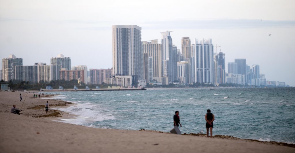 People stand on the shore in front of the skyline of Miami Beach, Florida, U.S., on Wednesday, Feb. 20, 2013. Photographer: Ty Wright/Bloomberg