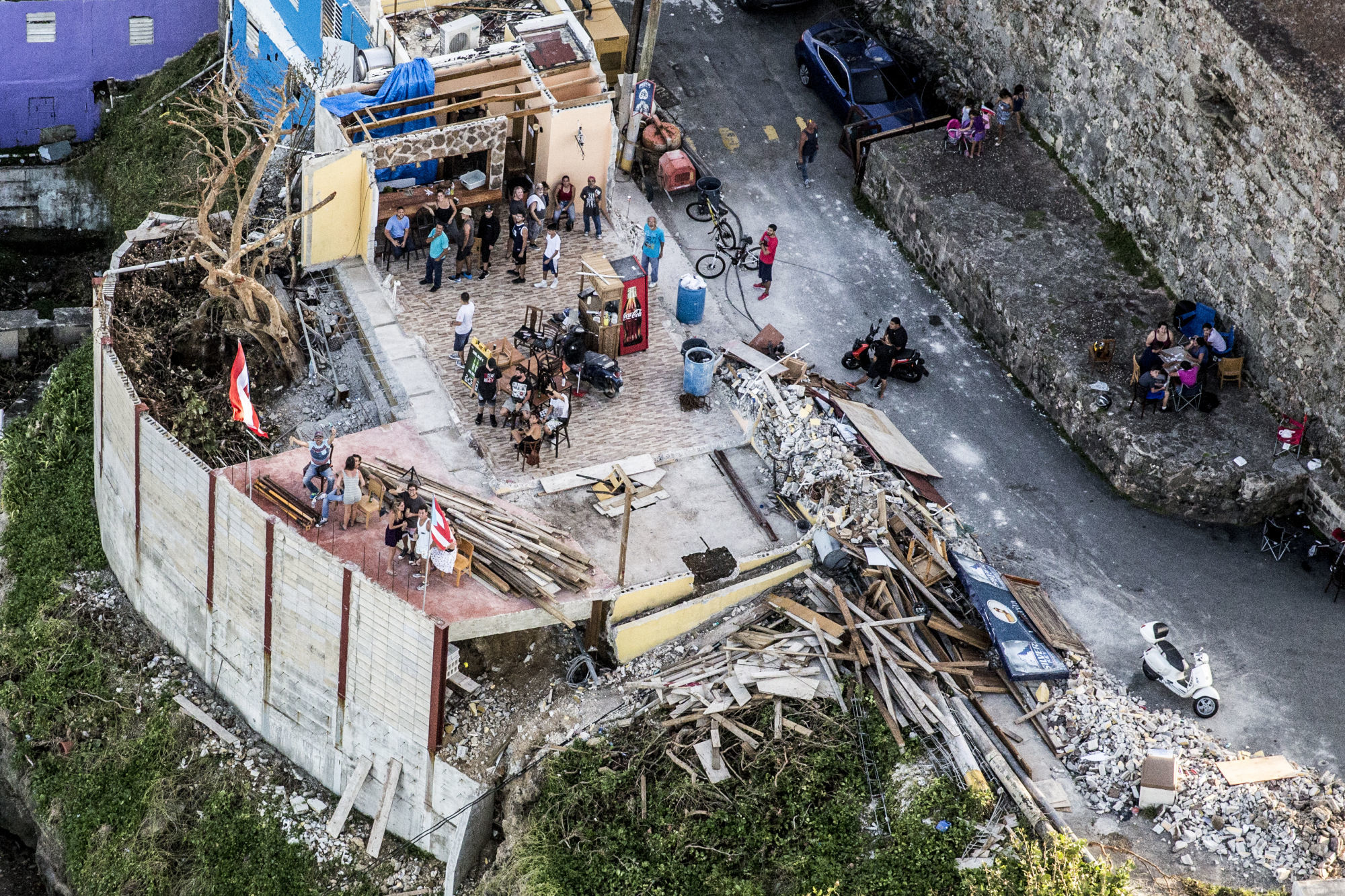People stand in a bar damaged from Hurricane Maria in this aerial photograph taken above La Perla, San Juan, Puerto Rico, on Monday, Sept. 25, 2017. Photographer: Alex Wroblewski/Bloomberg