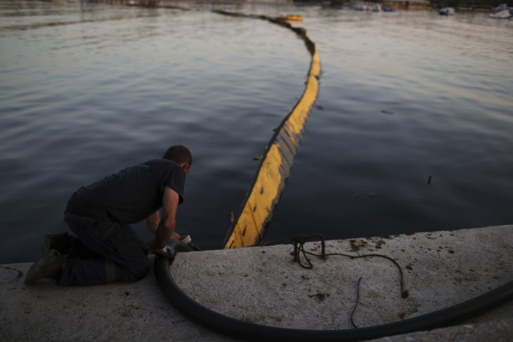 A worker from a cleaning company uses a hose to suck up polluted water from an oil spillage in front of a floating boom in Glyfada, suburb of Athens, on Monday, Sept. 18, 2017. The World Wildlife Fund has filed a lawsuit in Greece over extensive pollution along Athens' coastline following the sinking of a tanker near the country's largest port of Piraeus..