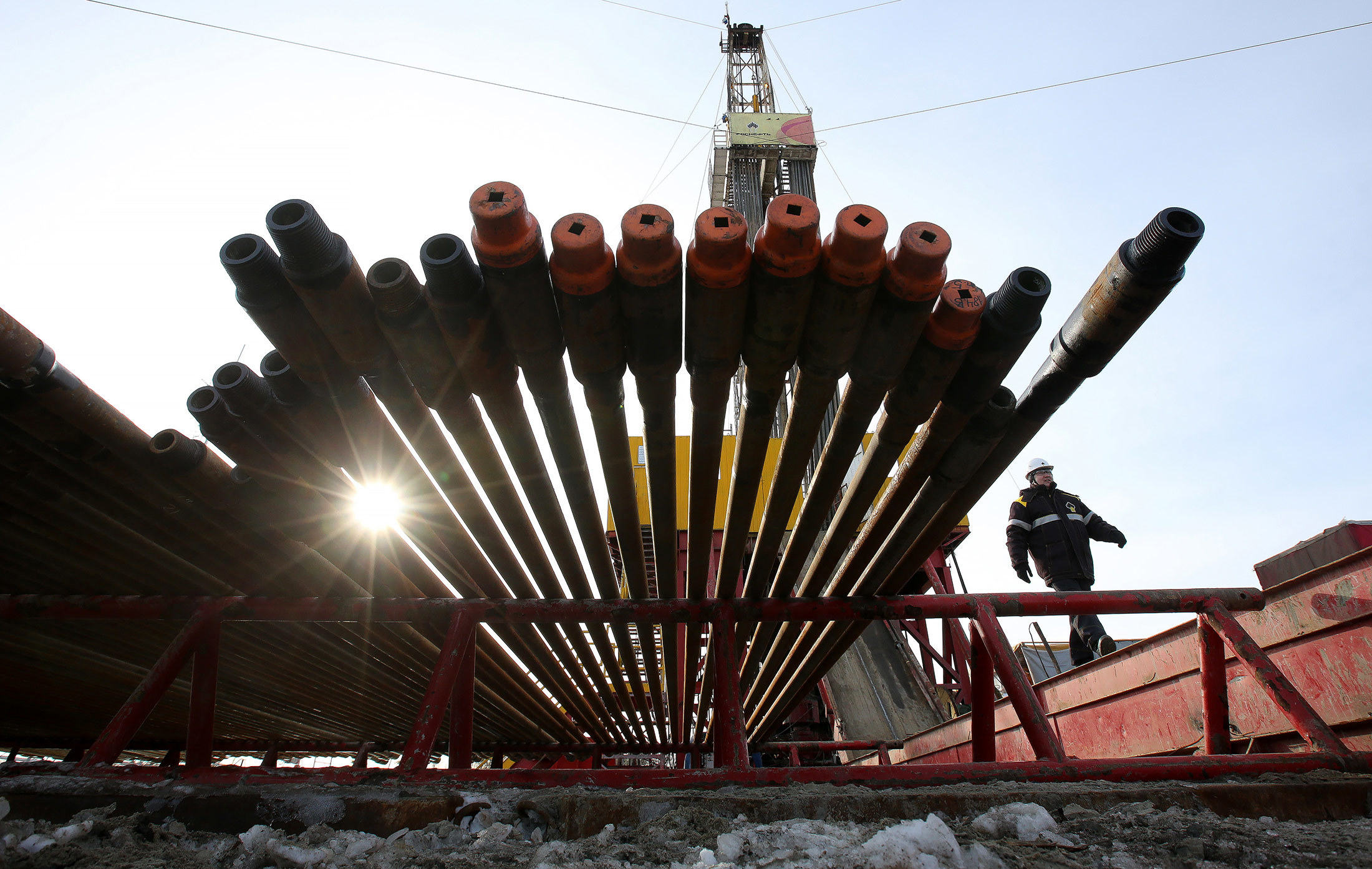 A worker passes an oil drilling rig and drill pipes, operated by Rosneft PJSC, in the Samotlor oilfield near Nizhnevartovsk, Russia, on Tuesday, March 21, 2017. Russia's largest oil field, so far past its prime that it now pumps almost 20 times more water than crude, could be on the verge of gushing profits again for Rosneft PJSC. Photographer: Andrey Rudakov/Bloomberg