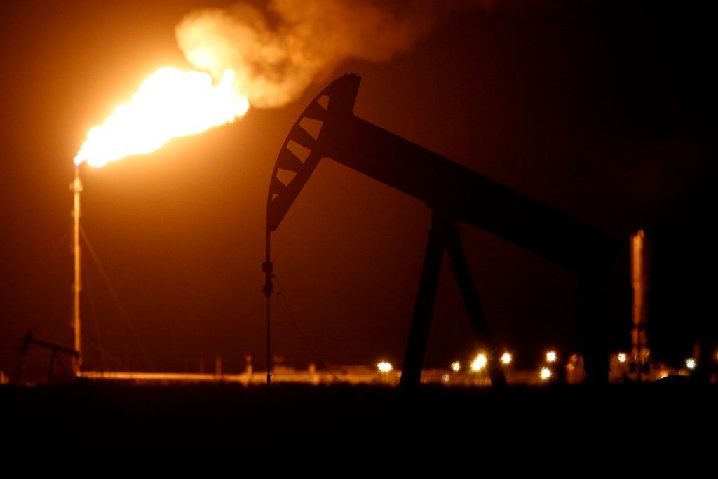 The silhouette of an electric oil pump jack is seen near a flare at night in the oil fields surrounding Midland, Texas