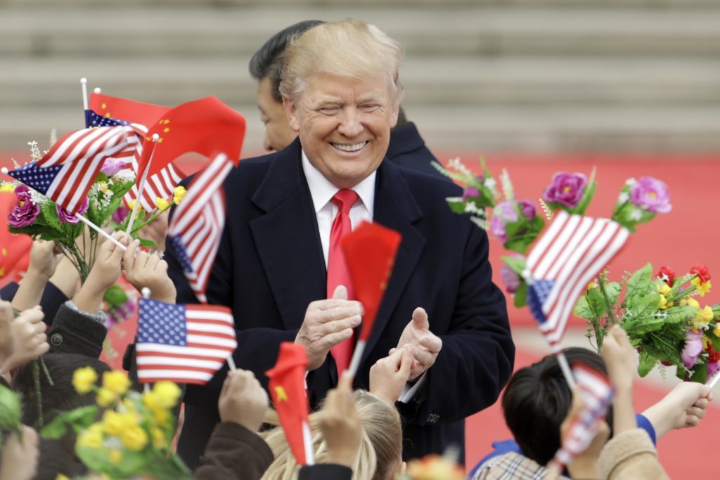 U.S. President Donald Trump, center, and Xi Jinping, China's president, greet attendees waving American and Chinese national flags during a welcome ceremony outside the Great Hall of the People in Beijing