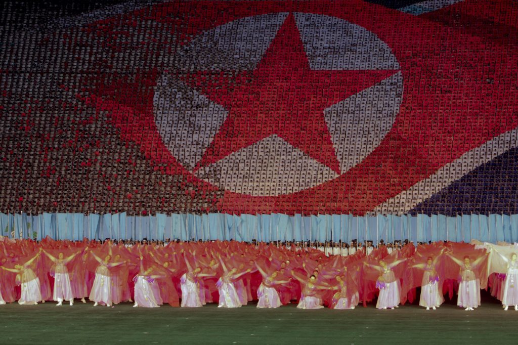 Performers dance in front of a depiction of the North Korean flag in Rungrado May Day Stadium during a ceremony commemorating the 65th anniversary of the Korea Worker's Party in Pyongyang, North Korea. Photographer: Bloomberg/Bloomberg