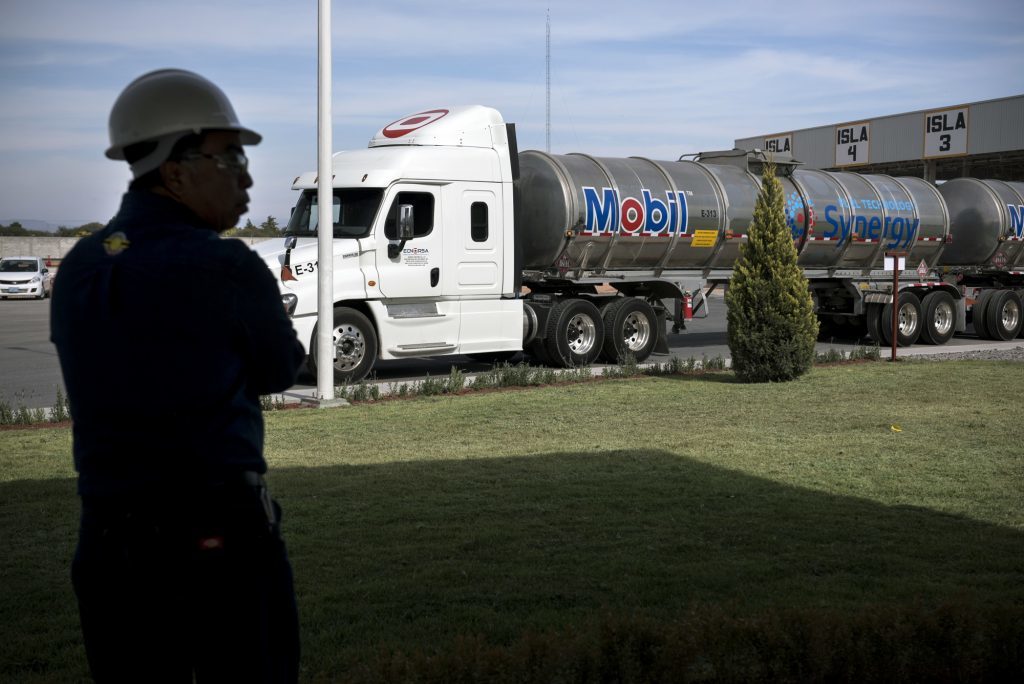 An employee stands in front of a fuel tanker during the unveiling of the Exxon Mobil Corp. fuel terminal in San Jose Iturbide, Mexico, on Wednesday, Dec. 6, 2017. Exxon Mobil Corp. is joining Chevron Corp. and other U.S. refiners to supply the newly free Mexican fuel market. Exxon Mobil indicated Wednesday that it will open 50 service stations by the end of first quarter and invest more than $300 million in Mexico's energy sector. Photographer: Jonathan Levinson/Bloomberg