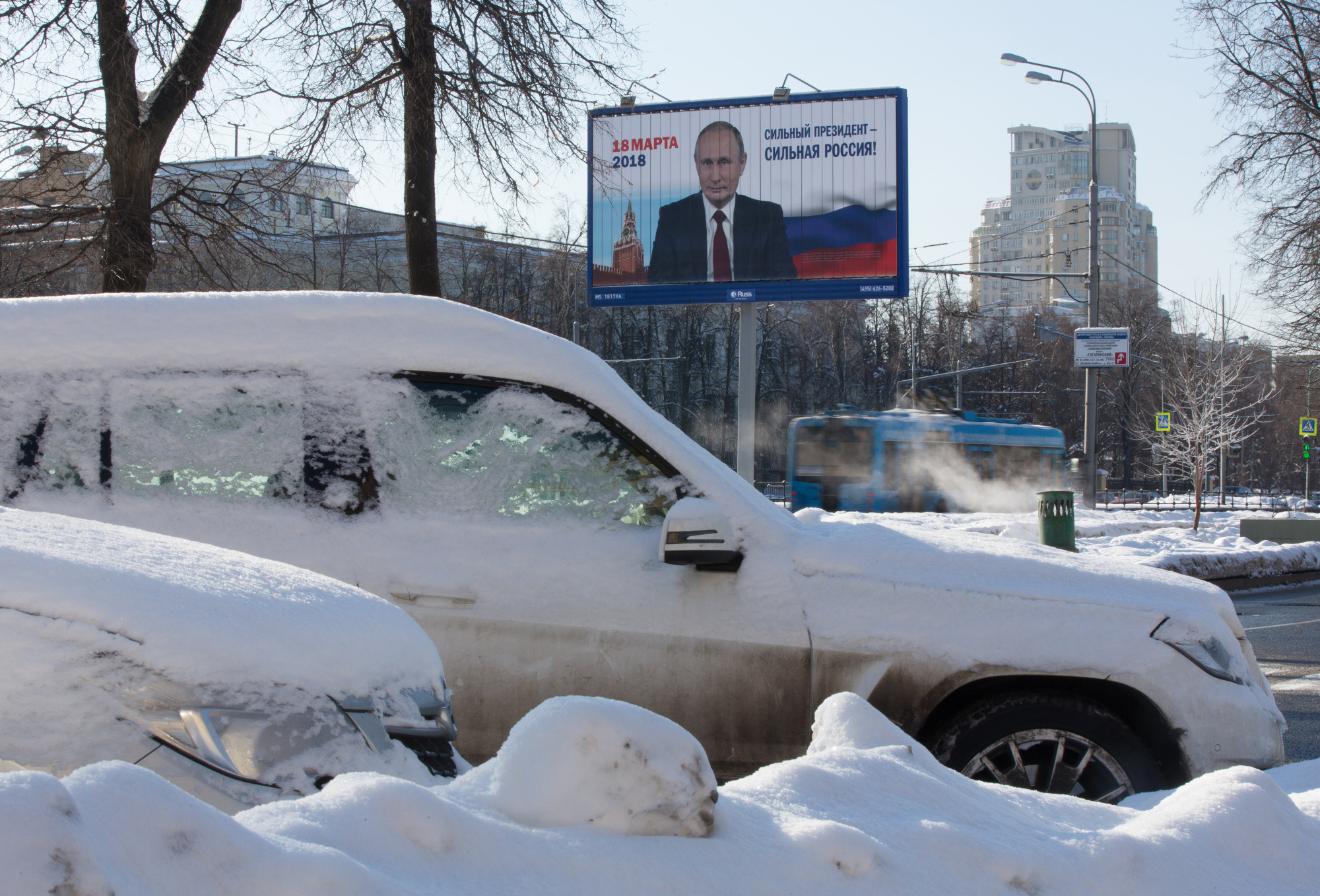 An election campaign billboard poster featuring incumbent Russian President Vladimir Putin stands beyond snow covered automobiles in Moscow, Russia. Photographer: Andrey Rudakov/Bloomberg