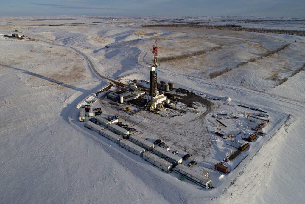 A Unit Drilling Co. rig stands in the Bakken Formation in this aerial photograph outside Watford City, North Dakota, U.S., on Friday, March 9, 2018. When oil sold for $100 a barrel, many oil towns dotting the nation's shale basins grew faster than its infrastructure and services could handle. Since 2015, as oil prices floundered, Williston has added new roads, including a truck route around the city, two new fire stations, expanded the landfill, opened a new waste water treatment plant and started work on an airport relocation and expansion project. Photographer: Daniel Acker/Bloomberg