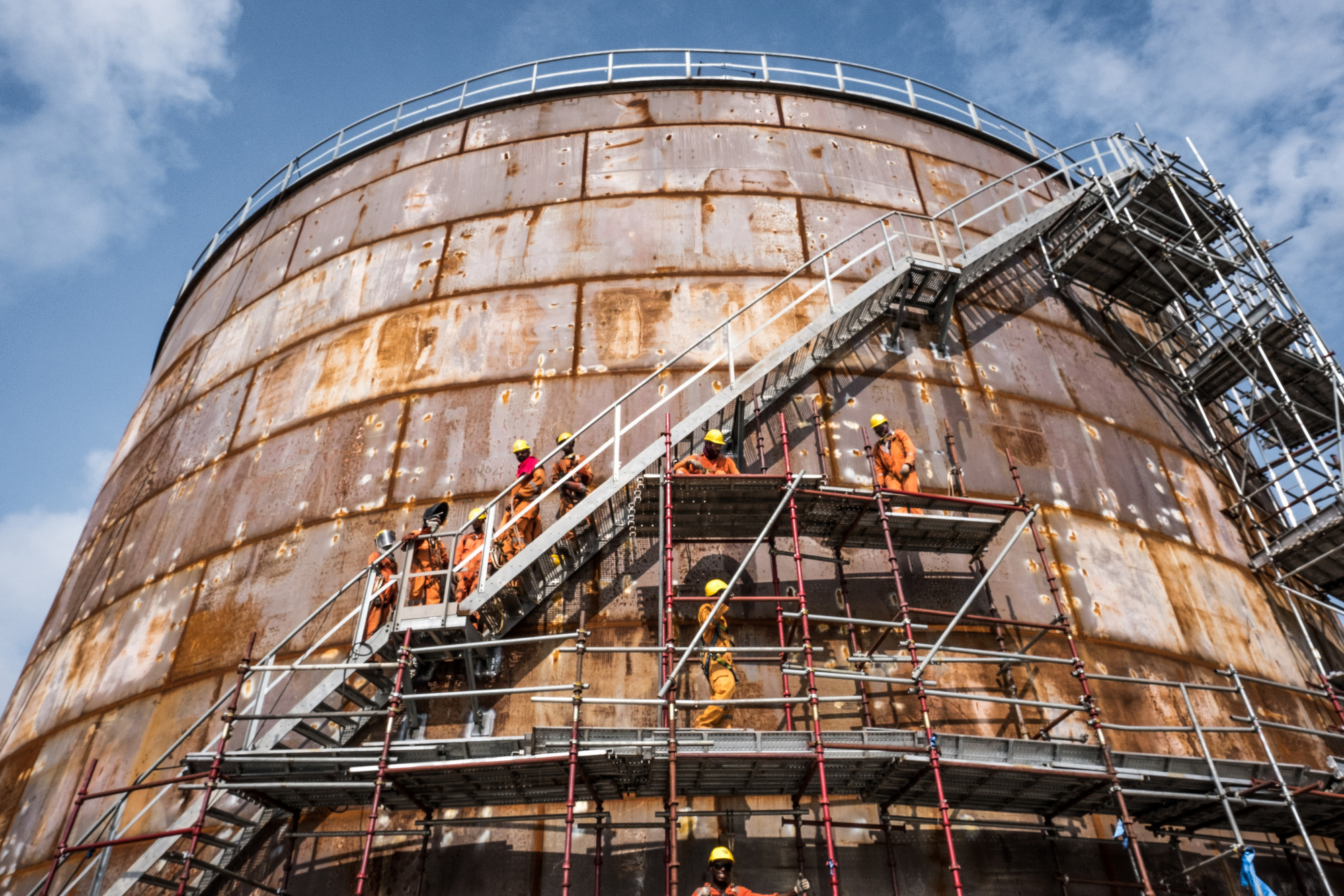 Workers climb scaffolding surrounding a storage tank at the under-construction Dangote Industries Ltd. oil refinery and fertilizer plant site in the Ibeju Lekki district, outside of Lagos, Nigeria, on Thursday, July 5, 2018. The $10 billion refinery, set to be one of the worlds largest and process 650,000 barrels of crude a day, should be near full capacity by mid-2020, Devakumar Edwin, group executive director at Dangote Industries said in an interview. Photographer: Tom Saater/Bloomberg