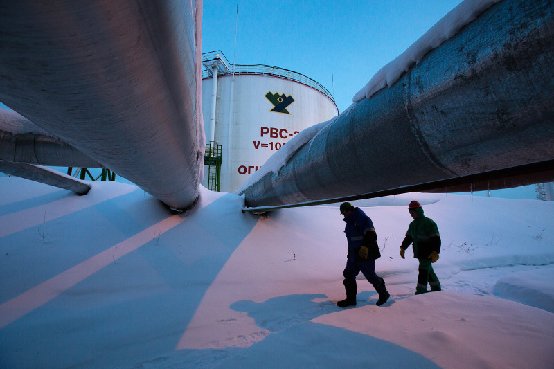 Employees pass beneath pipes leading to oil storage tanks at the central processing plant for oil and gas at the Salym Petroleum Development oil fields near the Bazhenov shale formation in Salym, Russia.Photographer: Andrey Rudakov/Bloomberg