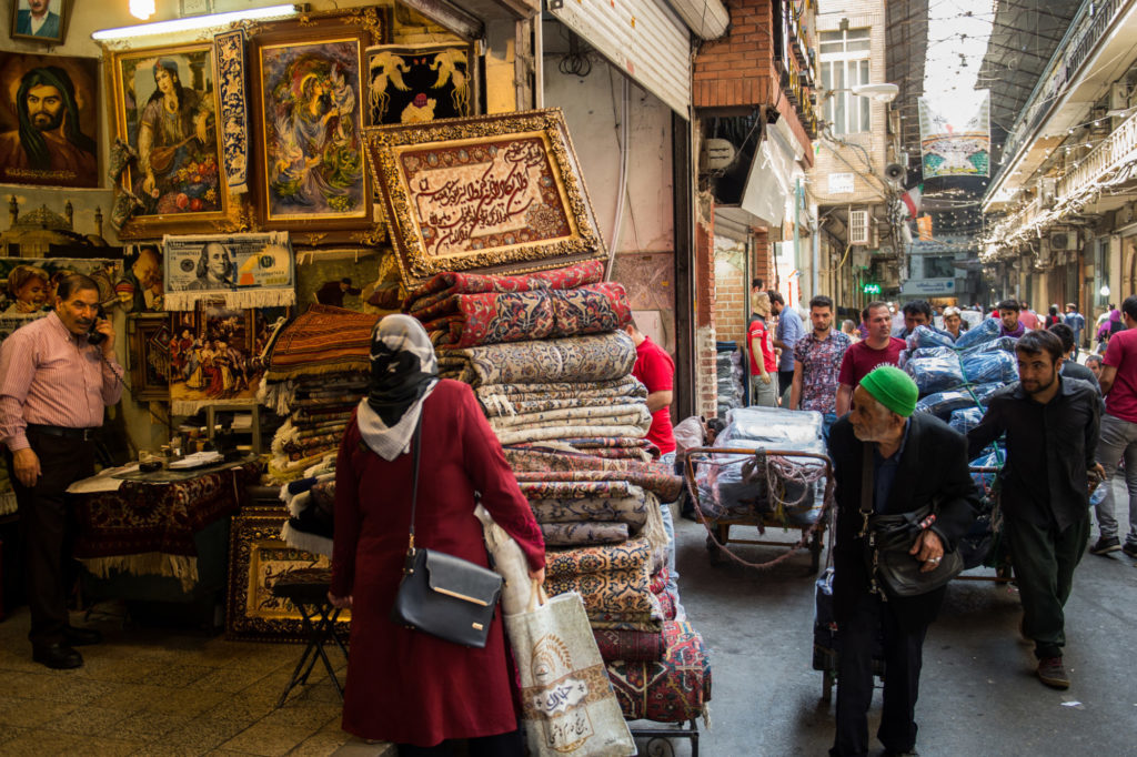Carpet traders wheel their wares past a store selling Persian rugs inside the Grand Bazaar in Tehran, on Aug. 6. Photographer: Ali Mohammadi/Bloomberg
