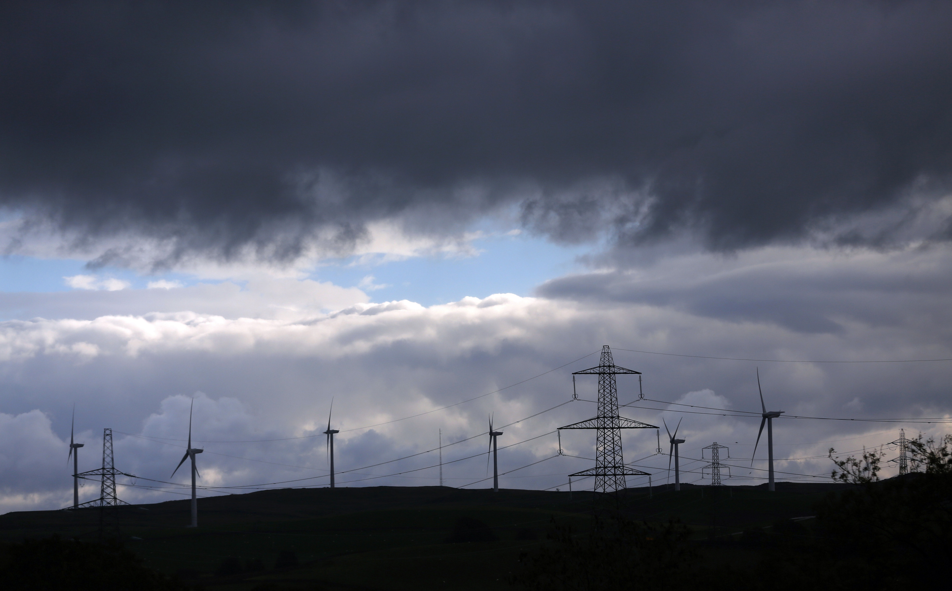 Wind turbines stand on the horizon near a National Grid Plc electricity pylons in Kendal, U.K. Photographer: Paul Thomas/Bloomberg