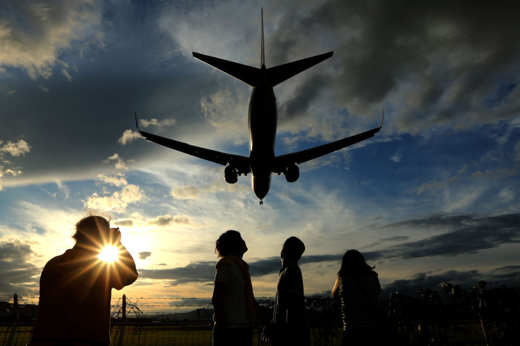People watch a Japan Airlines Corp. (JAL) aircraft approaching to land at the Osaka International Airport, operated by New Kansai International Airport Co., in Toyonaka City, Osaka, Japan. Photographer:Buddhika Weerasinghe/ Bloomberg
