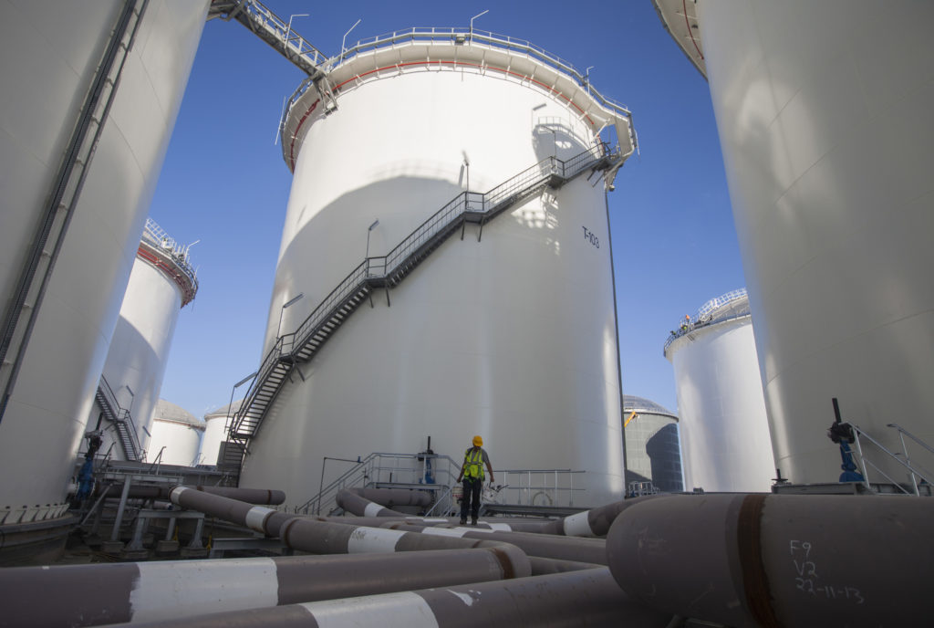 A construction worker stands on pipes at the base of fuel storage tanks. Photographer: Andrew Caballero-Reynolds