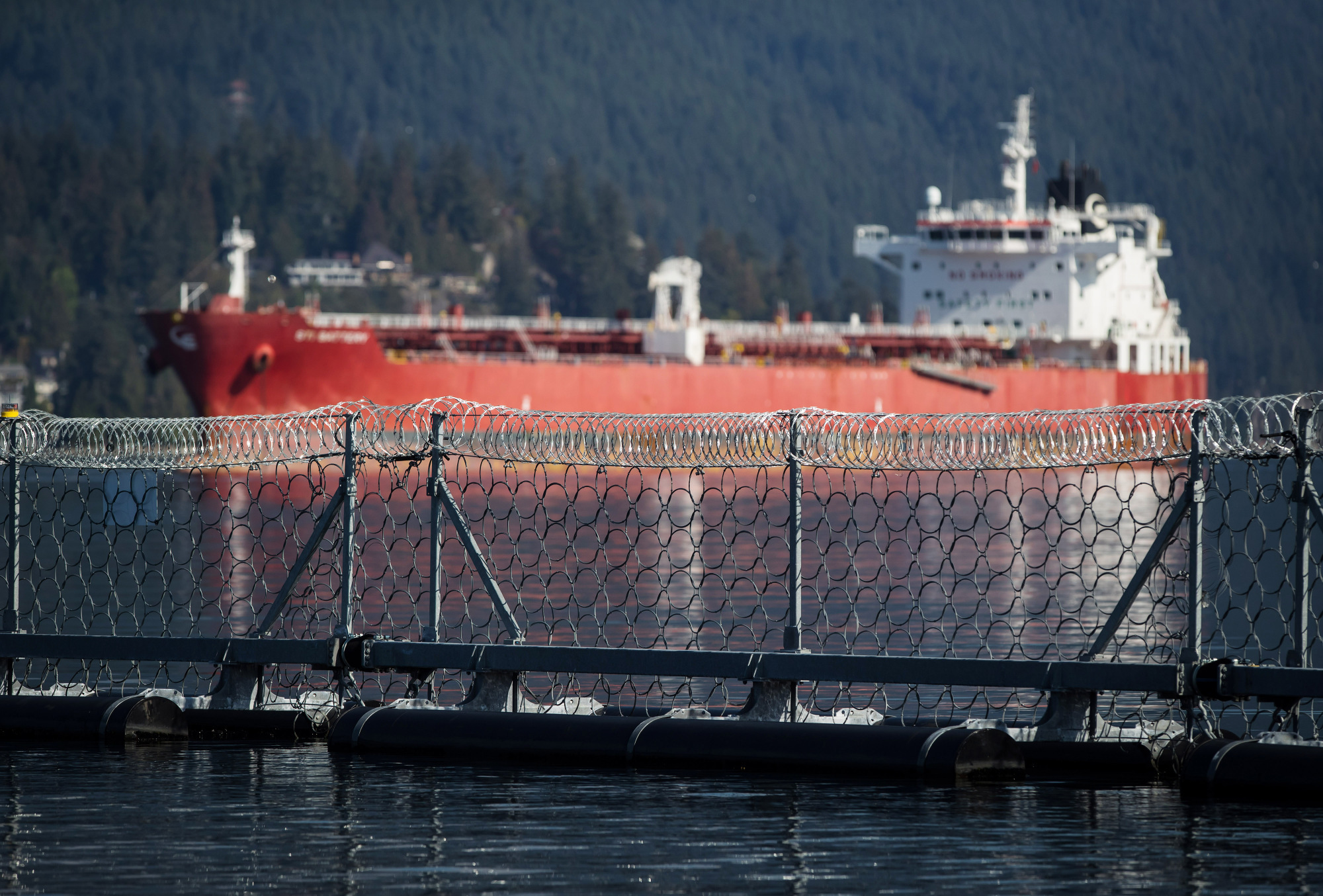 A razor wire security fence floats in front of the STI Battery oil and chemical tanker during an emergency response exercise in Burrard Inlet at the Kinder Morgan Inc. Westridge Marine Terminal in Burnaby, British Columbia, Canada, on Wednesday, Sept. 19, 2018. A Canadian court's decision to nullify approval of the Trans Mountain Expansion Project will increase crude-by-rail transport in the near term and will likely have a "negative impact on Canadian output growth in the longer term," the International Energy Agency said earlier this month. Photographer: Darryl Dyck/Bloomberg