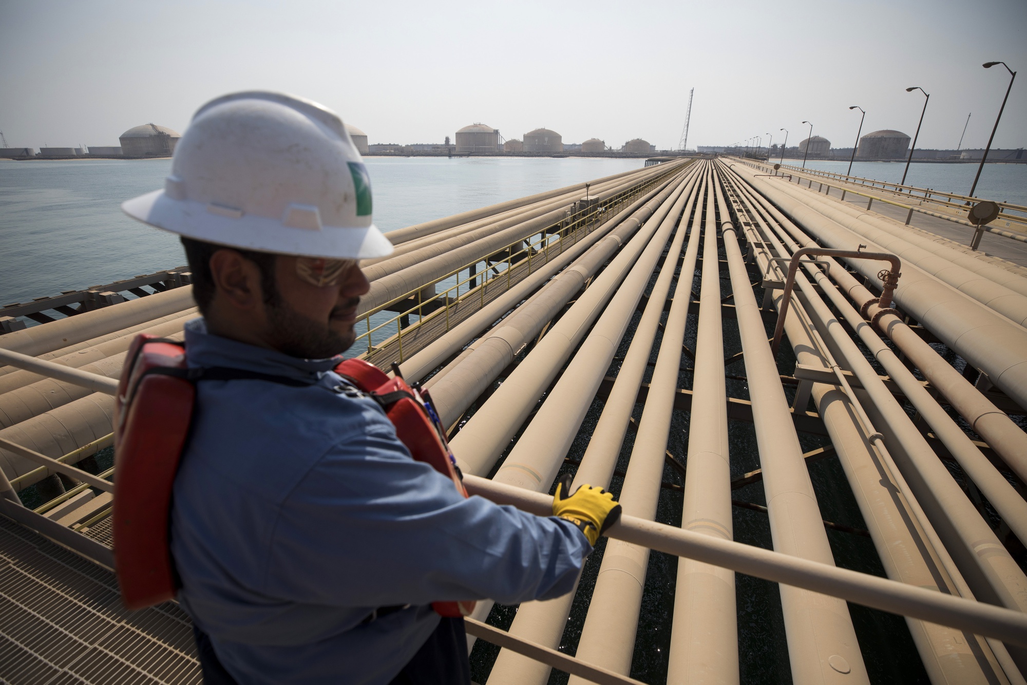 An employee looks out over oil transport pipelines on the Arabian Sea in Saudi Aramco's Ras Tanura oil refinery and oil terminal in Ras Tanura, Saudi Arabia. Photographer: Simon Dawson/Bloomberg