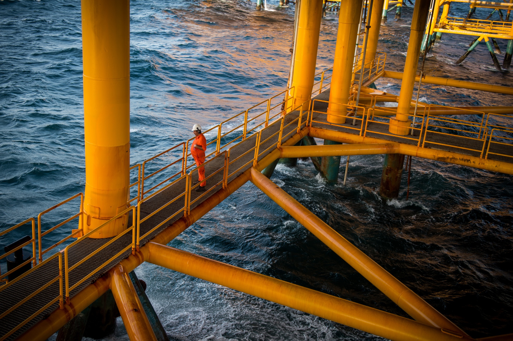 A worker looks out to sea from a low walkway aboard an offshore oil platform in the Persian Gulf's Salman Oil Field, operated by the National Iranian Offshore Oil Co., near Lavan island, Iran. Photographer: Ali Mohammadi/Bloomberg