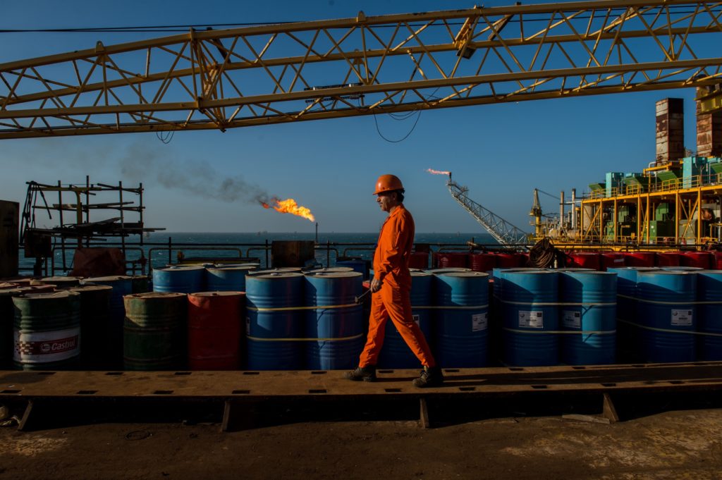 A worker passes stores of oil drums and gas flares while working aboard an offshore oil platform in the Persian Gulf's Salman Oil Field, operated by the National Iranian Offshore Oil Co., near Lavan island, Iran, on Friday, Jan. 6. 2017. Nov. 5 is the day when sweeping U.S. sanctions on Irans energy and banking sectors go back into effect after Trumps decision in May to walk away from the six-nation deal with Iran that suspended them. Photographer: Ali Mohammadi/Bloomberg