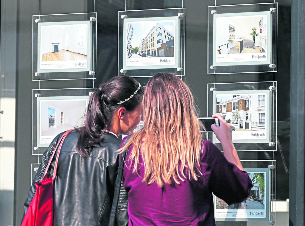 Two women looking at houses for sale in an estate agent's window.