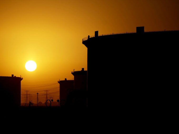The sun sets beyond crude oil storage tanks at the Juaymah tank farm at Saudi Aramco's Ras Tanura oil refinery and oil terminal in Ras Tanura, Saudi Arabia. Photographer: Simon Dawson