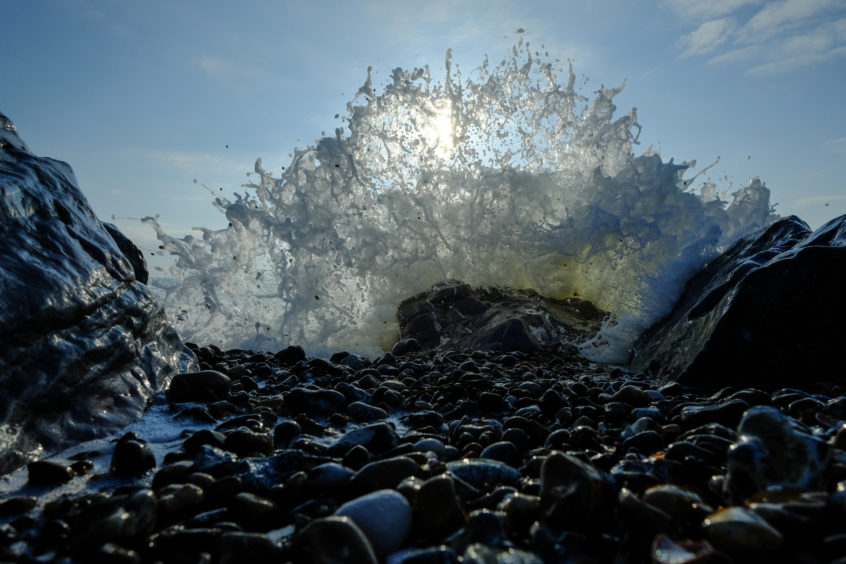 Crashing wave against a rock with the sunshine behind