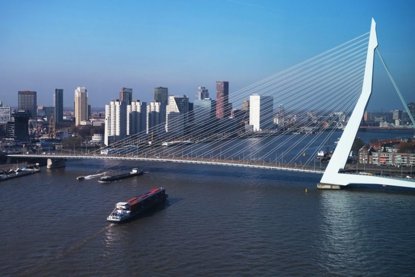 A ship goes under a bridge with a city scape behind