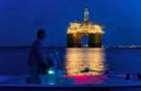 A lit up platform on water while a boater is silhouetted against the dark blue sky