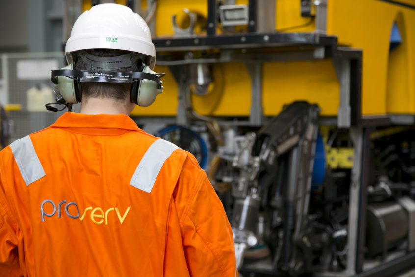 Man in orange overalls with back to camera looks at equipment