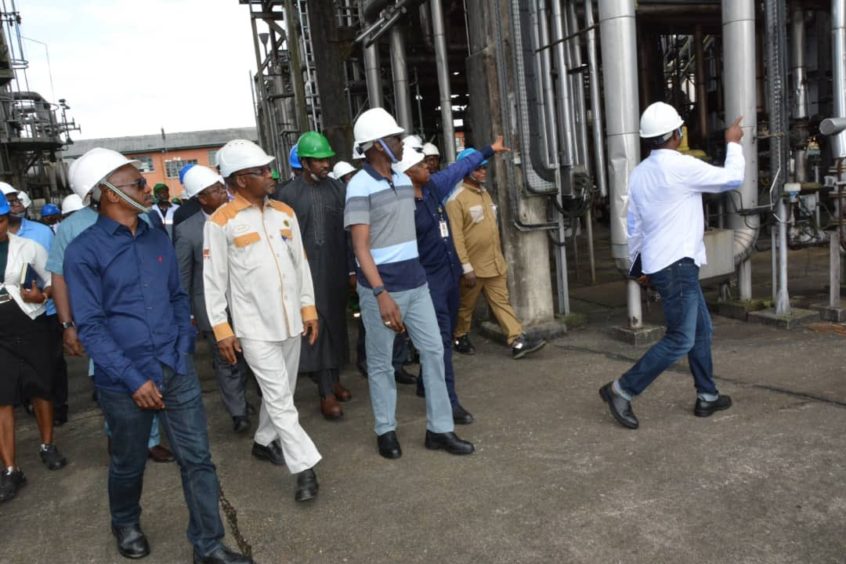 Group of men walk through industrial scene with pipes