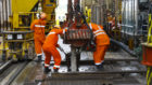 Workers in orange coveralls work on a pipe