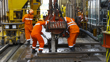 Workers in orange coveralls work on a pipe