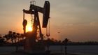 A silhouetted pump jack with trees on the horizon