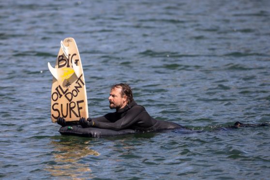 A man holds up a board reading "Big oil don't surf" during a surf demonstration, a so-called paddle-out, taking place on May 12, 2019 in the harbor pool outside the Opera House in Oslo, Norway. - The surfers demonstrate against a planned oil exploration of Norwegian multinational energy company Equinor in the The Great Australian Bight. (Photo by Ola Vatn / NTB Scanpix / AFP) / Norway OUT (Photo credit should read OLA VATN/AFP via Getty Images)