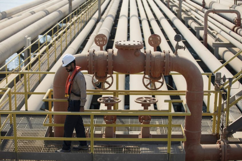 Pipelines recede into the distance, foreground to the left a man in a hard hat